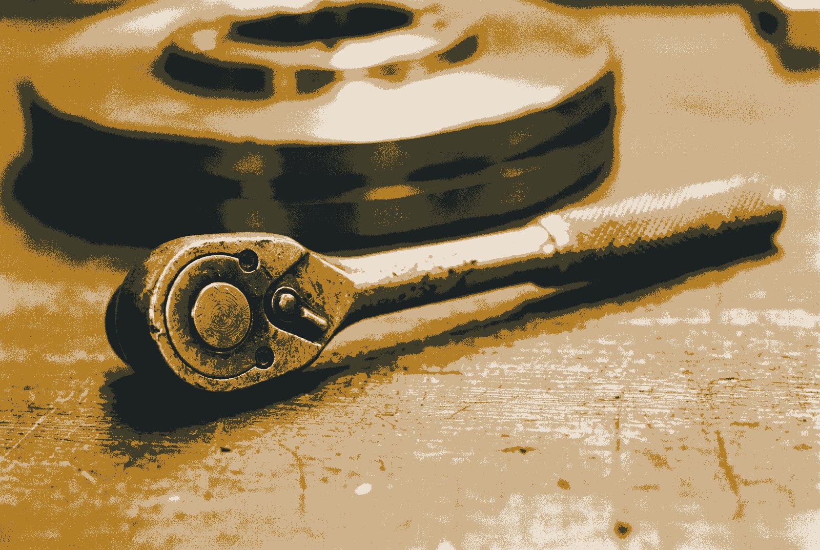 A socket ratchet spanner lying diagonally on a workbench, its direction lever in sharp focus, with a large soft circle behind it.