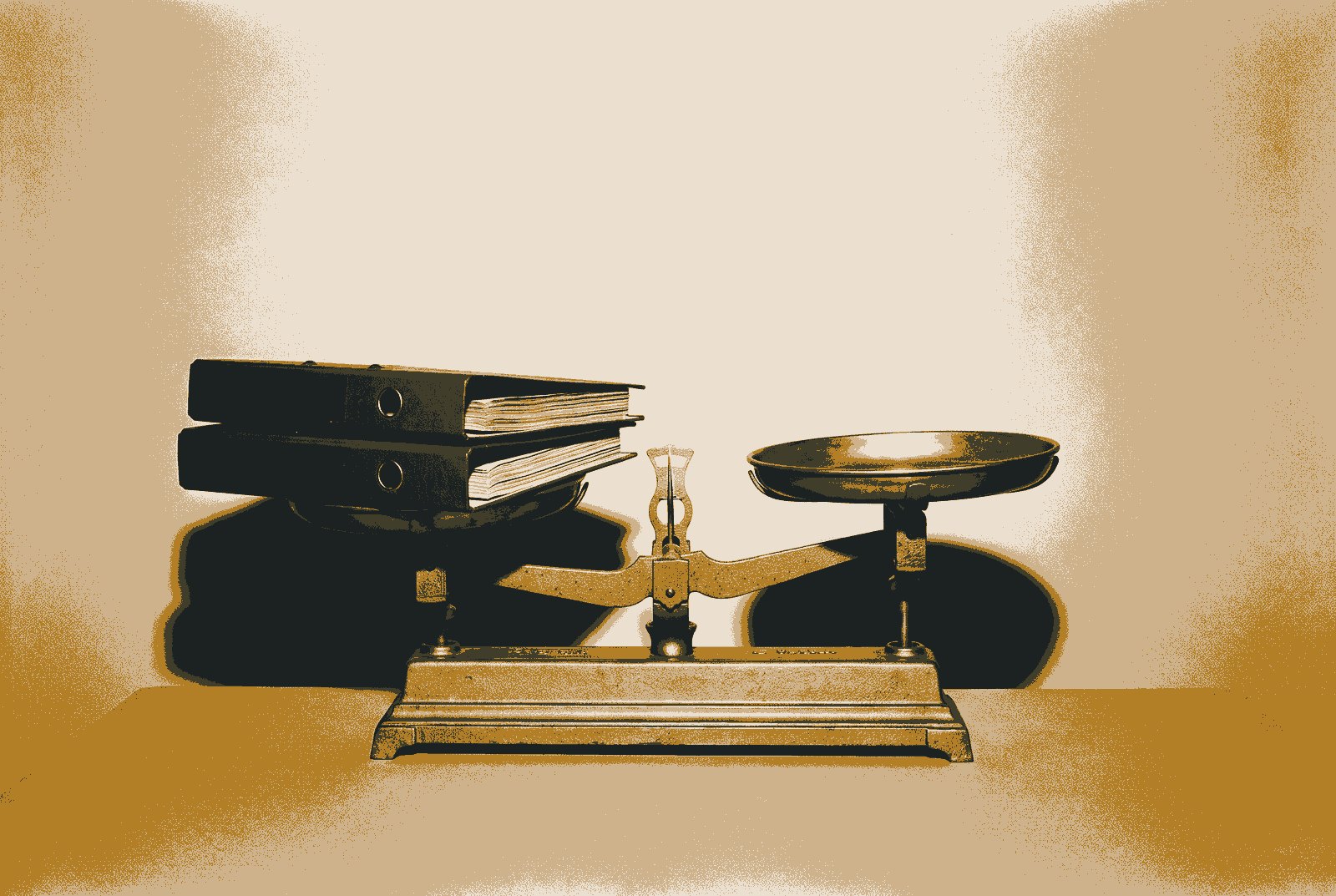A symmetrical two-pan balance scale with two thick binders stacked in one pan and the other pan empty and raised.