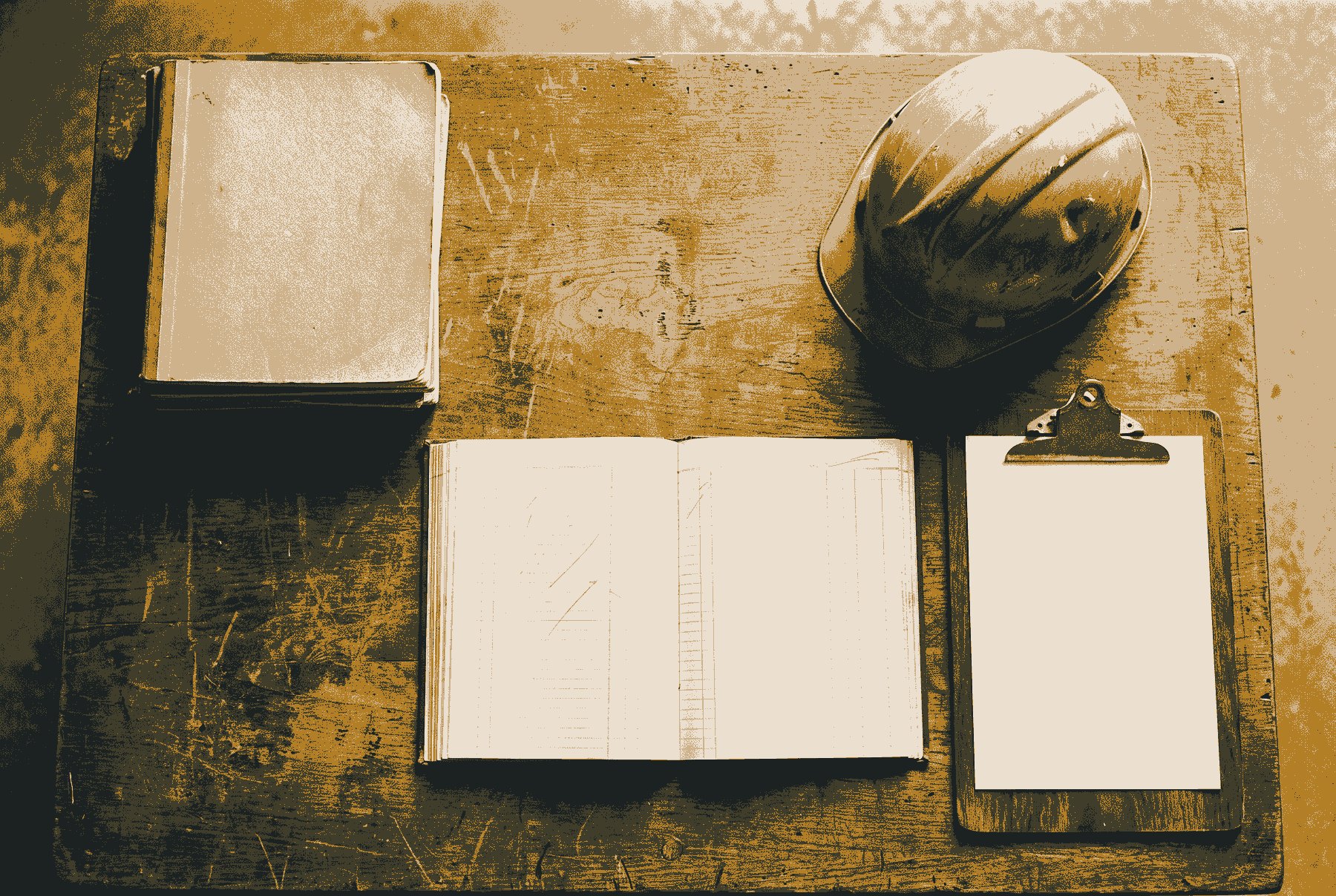 A site-office desk seen from above, with a stack of worn notebooks, an open ledger with faint pencil marks, a battered hard hat and an empty clipboard.